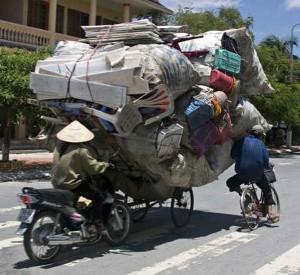 Overwhelmed bicyclists carrying mattresses and furniture on bike