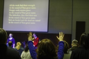 A worship with her hands in the air, in the midst of other worshipers at Sojourn New Albany Church.