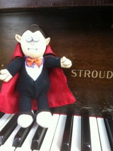 Stuffed vampire toy setting on the keys of a Stroud baby grand piano